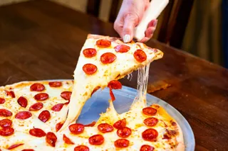 A hand pulling a cheesy slice of pepperoni pizza