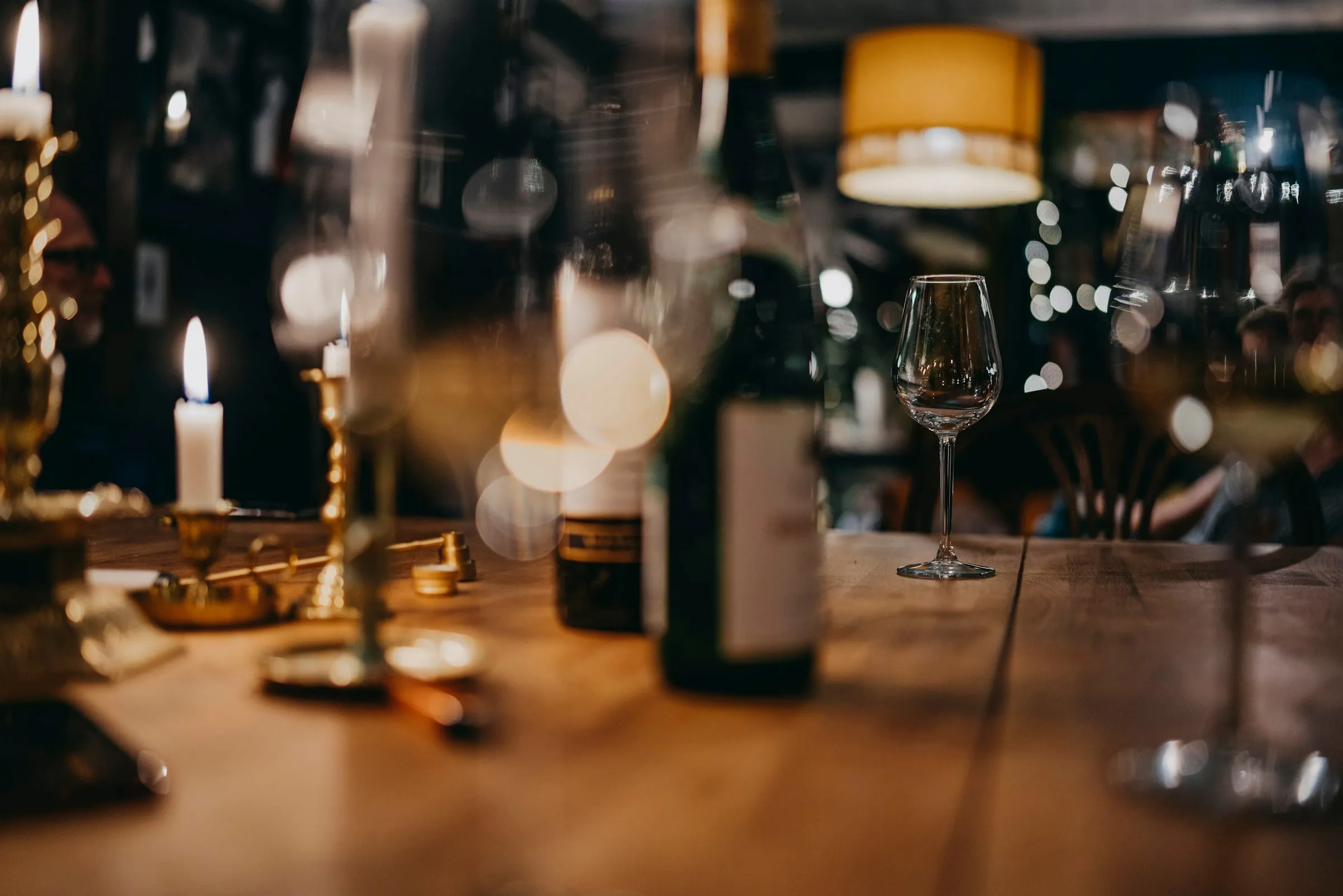 Candles and wine bottles on a long wooden table in a warmly lit bar