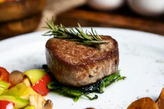 A filet topped with rosemary beside colorful vegetables
