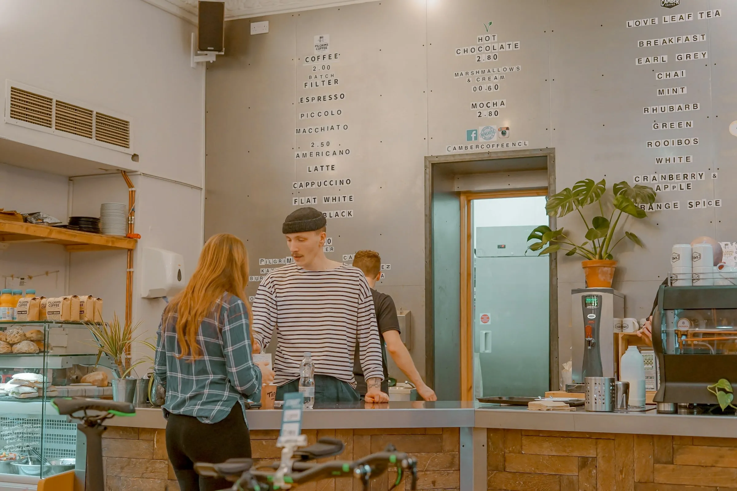 A bright coffee shop with customers ordering at a light wood counter