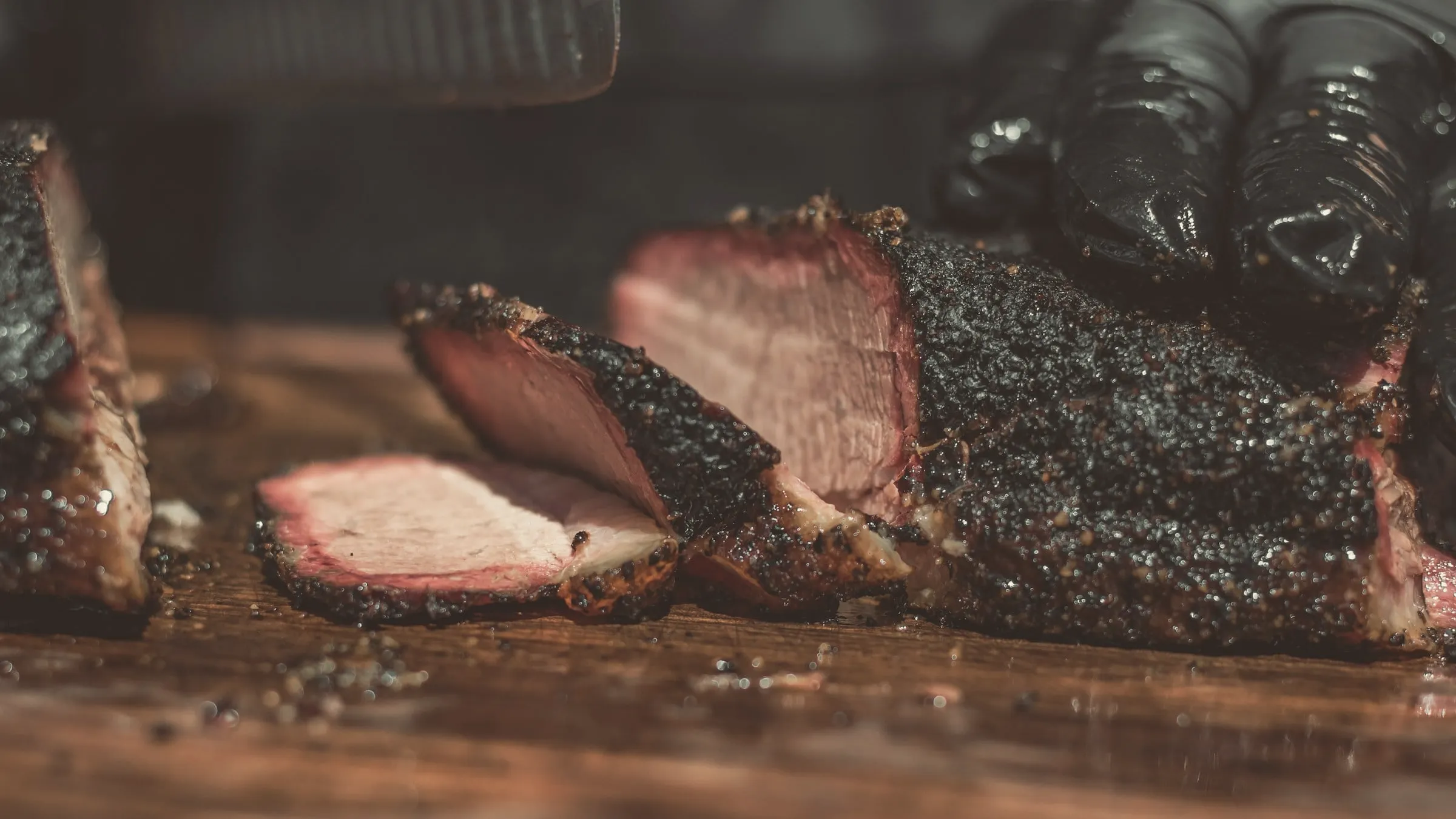 A whole smoked brisket with a dark bark, sliced on a wooden board