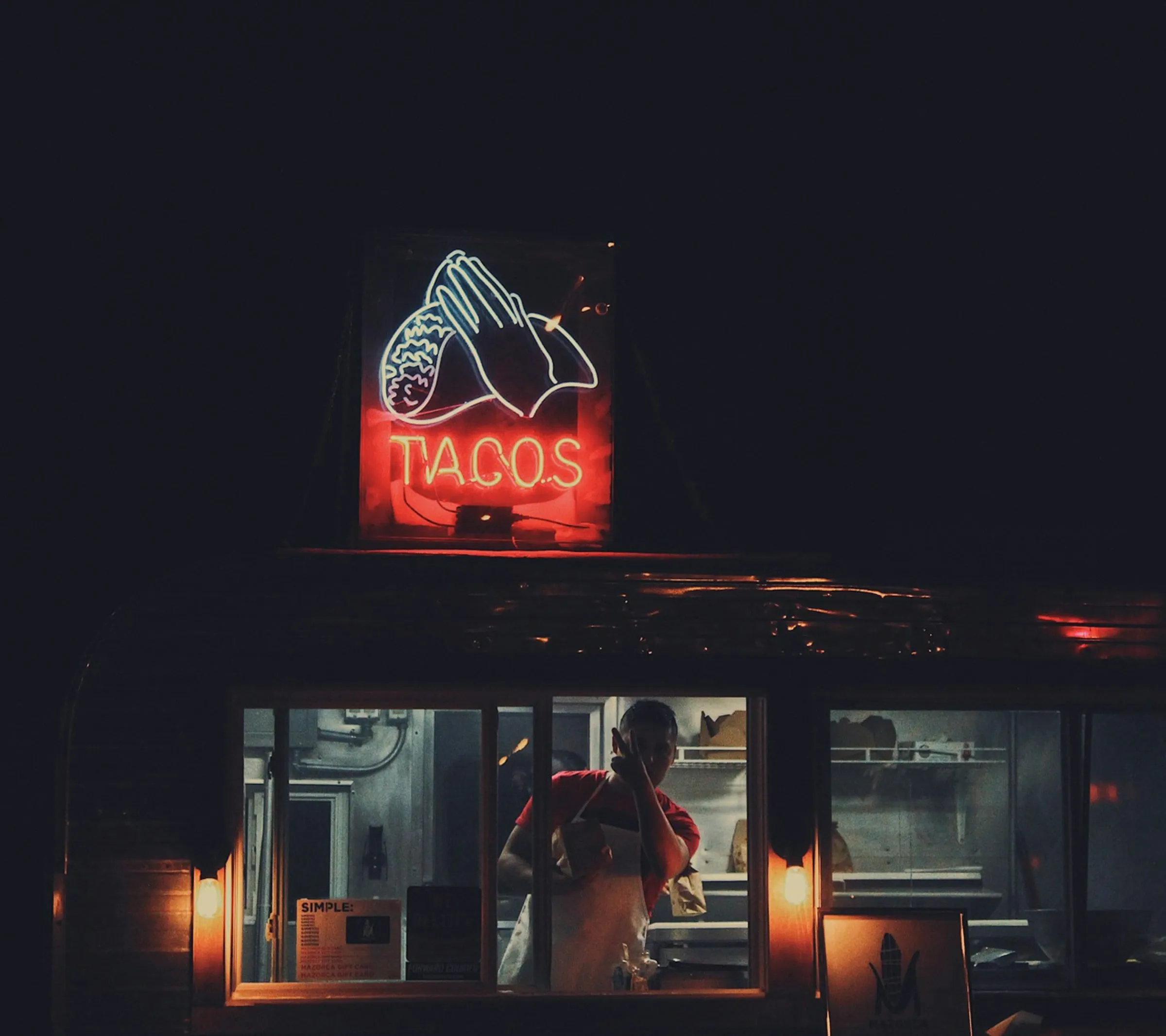 A red neon taco sign glowing above a walk-up window at night