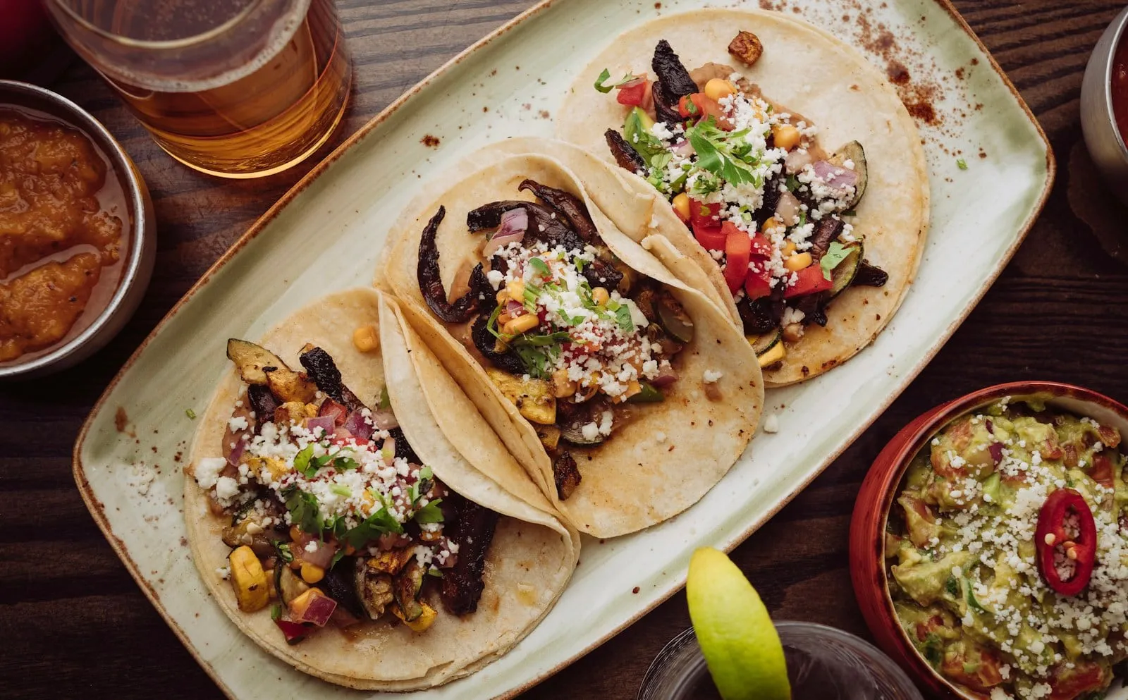 Three tacos on a long plate with a beer behind them