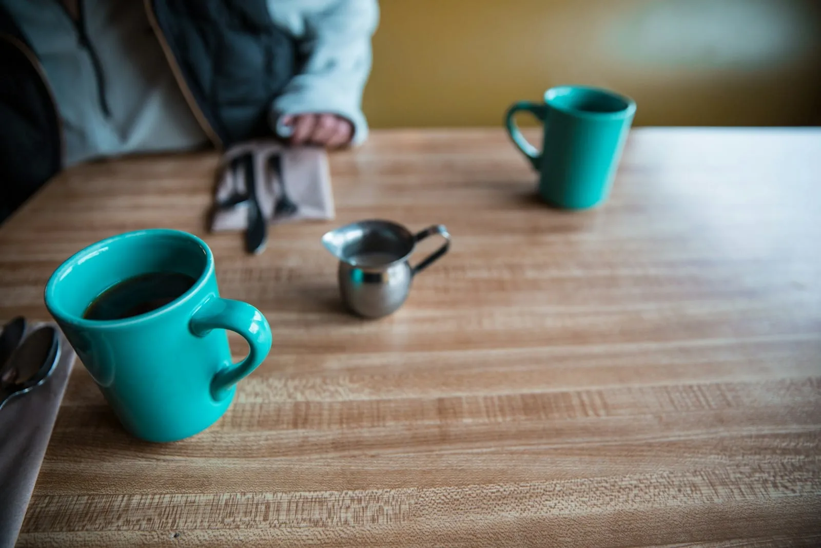 Two teal coffee mugs on a wooden table