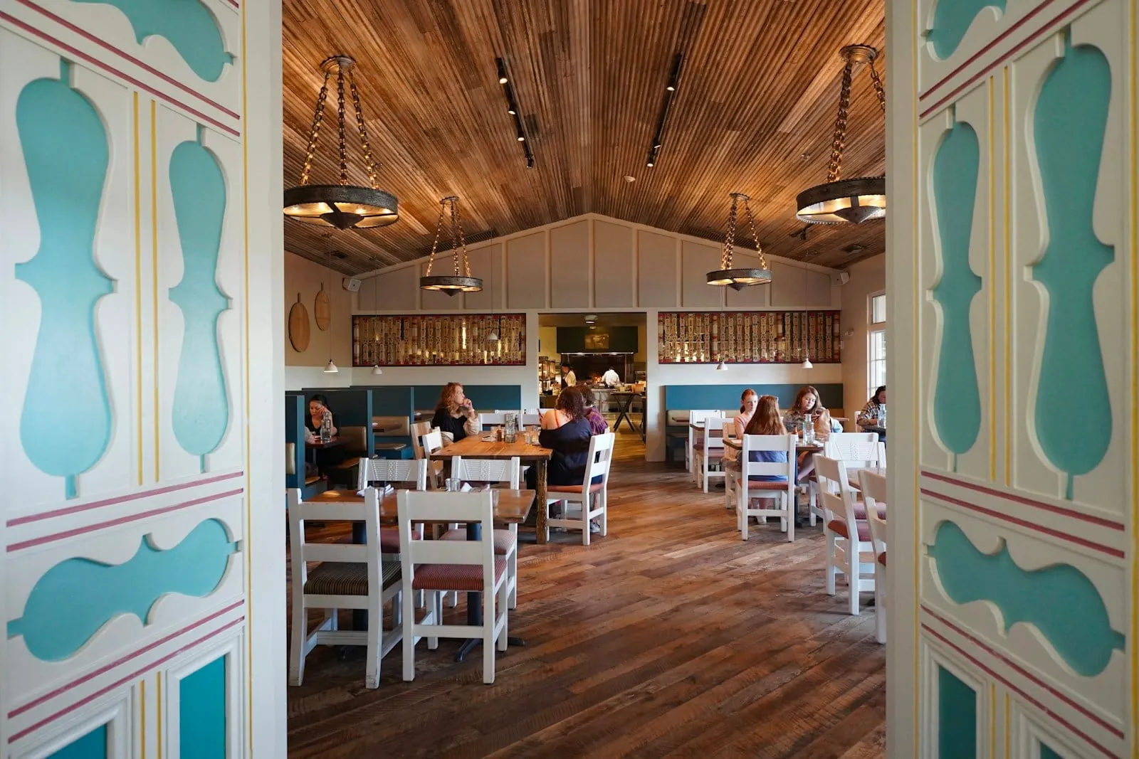 A bright farmhouse dining room with white chairs and a wood-plank ceiling