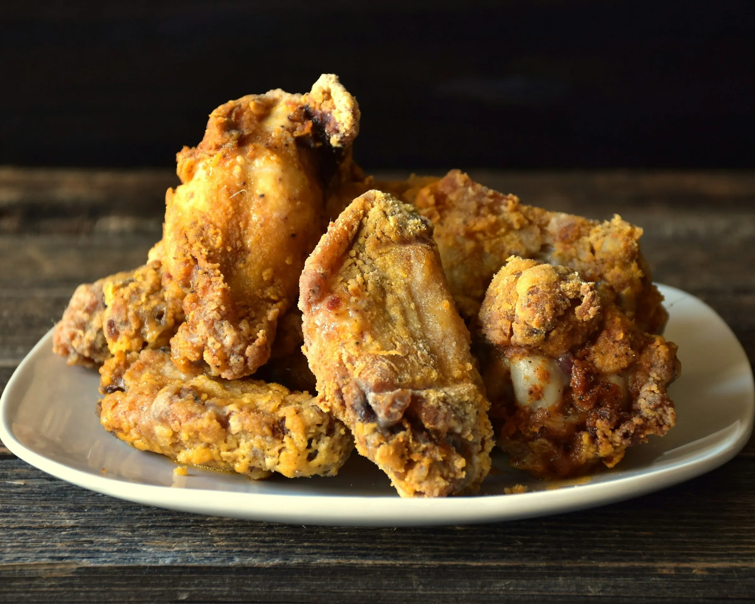 Golden buttermilk fried chicken piled on a white plate on a dark wooden table