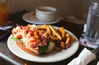 A lobster roll with fries on a white plate