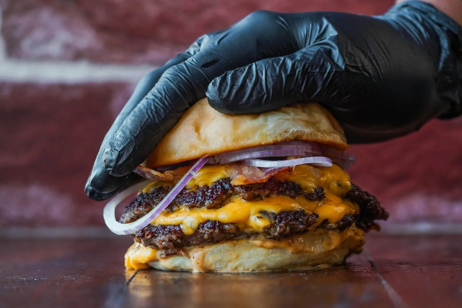A gloved hand pressing down on a double cheeseburger