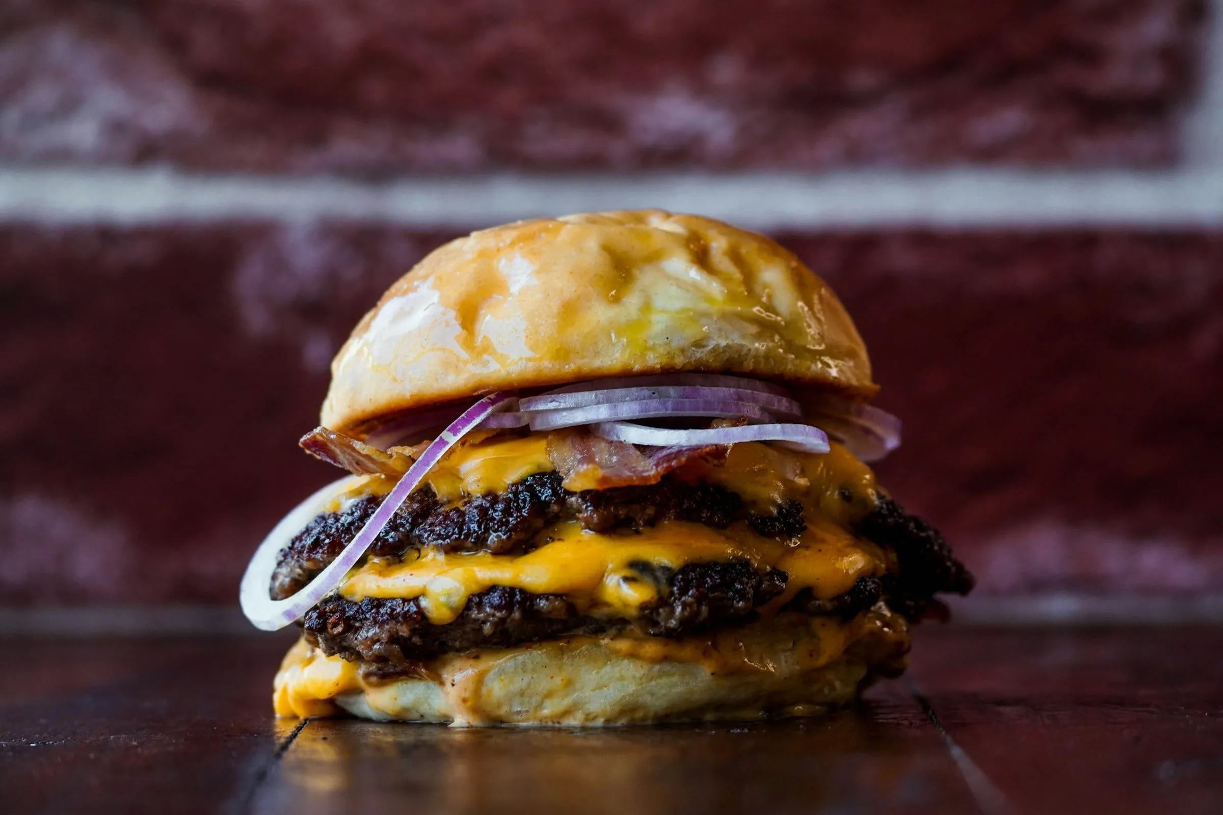 A double cheeseburger with grilled onions in front of a red brick wall