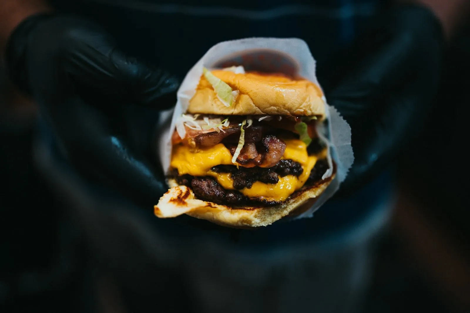 Two hands holding a cheeseburger wrapped in paper