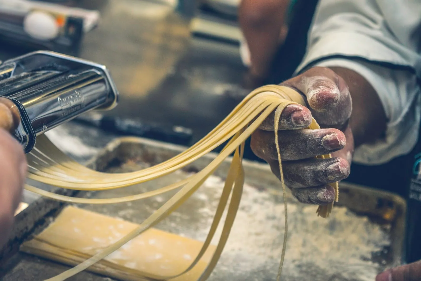 Hands feeding fresh pasta through a pasta machine