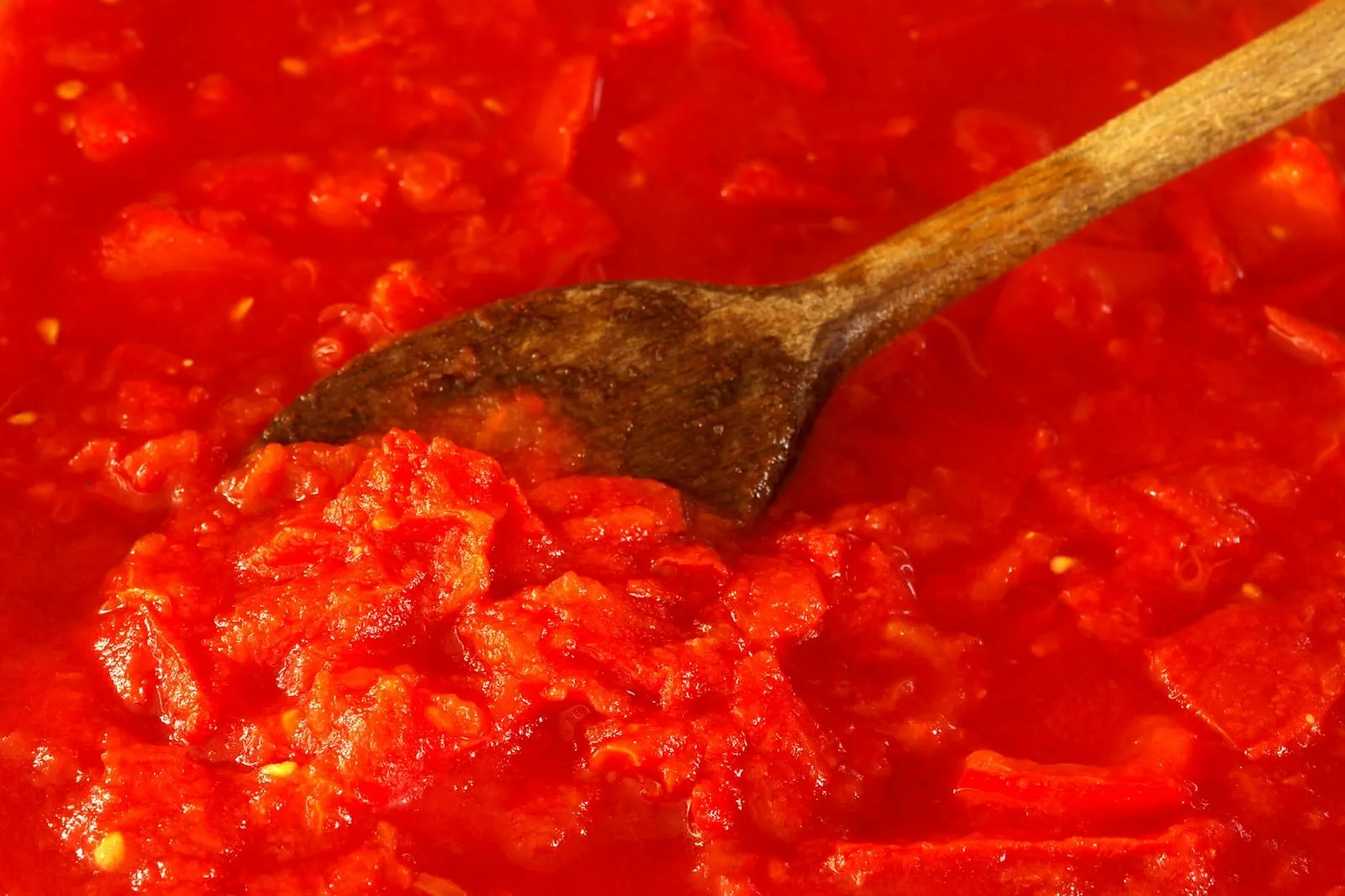 A wooden spoon stirring a rich tomato sauce